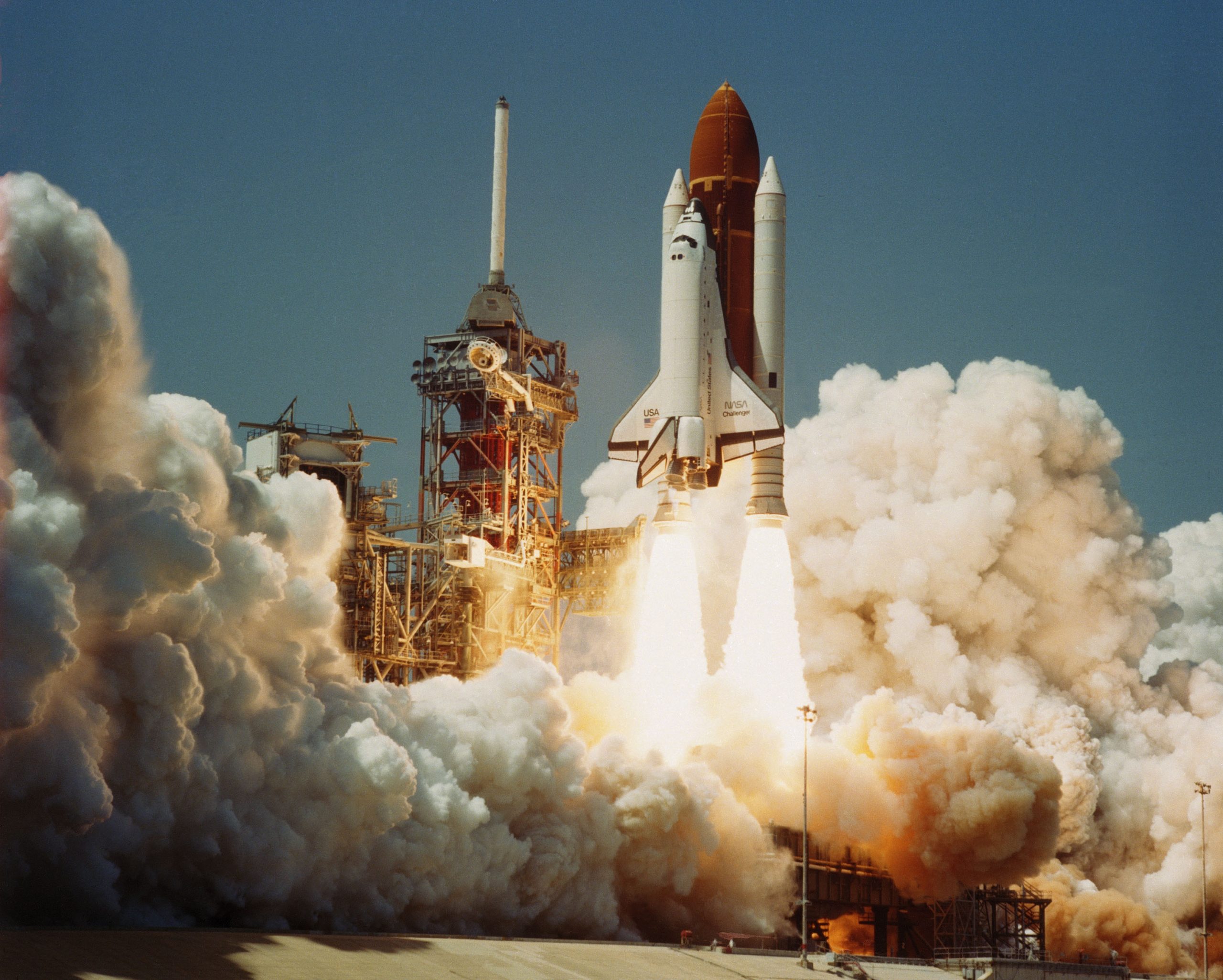 A space shuttle, the Challenger, in take off, showing flames exiting rockets and surrounded by billowing clouds created by smoke. Space Transportation System Number 6, Orbiter Challenger, lifts off from Pad 39A carrying astronauts Paul J. Weitz, Koral J. Bobko, Donald H. Peterson and Dr. Story Musgrave.