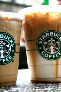  A photograph of two Starbucks drinks beside each other in clear cups on a table, with the Starbucks icon visible on both cups. The cup on the left is a smaller size and filled with light brown frozen coffee. The right cup has coffee in the top and cream in the bottom, with a gradient in between. 