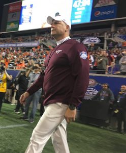 Virginia Tech Head football coach, Justin Fuente, walking across the field at night with fans in the stands.