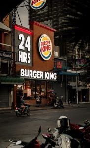 Picture of a Burger King restaurant at night. Modern building with an illuminated sign that says '24 HRS'.