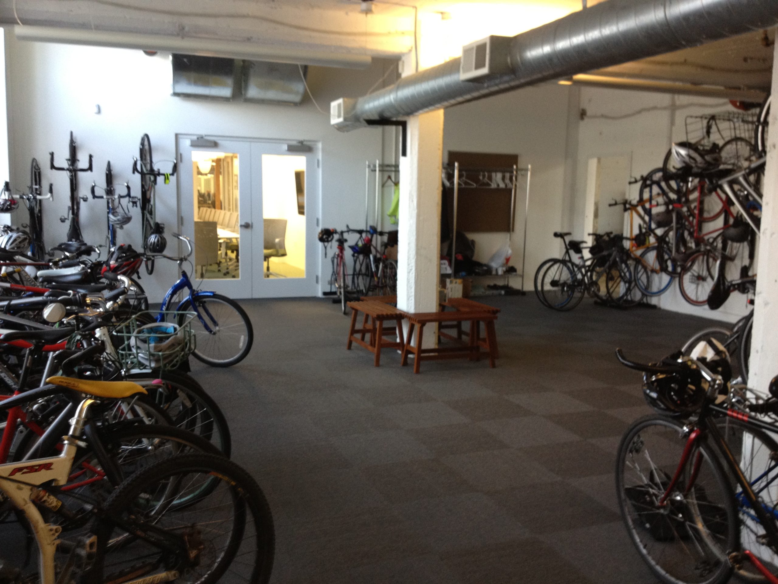 A room hiousing about 30 bikes. Some are on the ground and some are hanging on the walls.