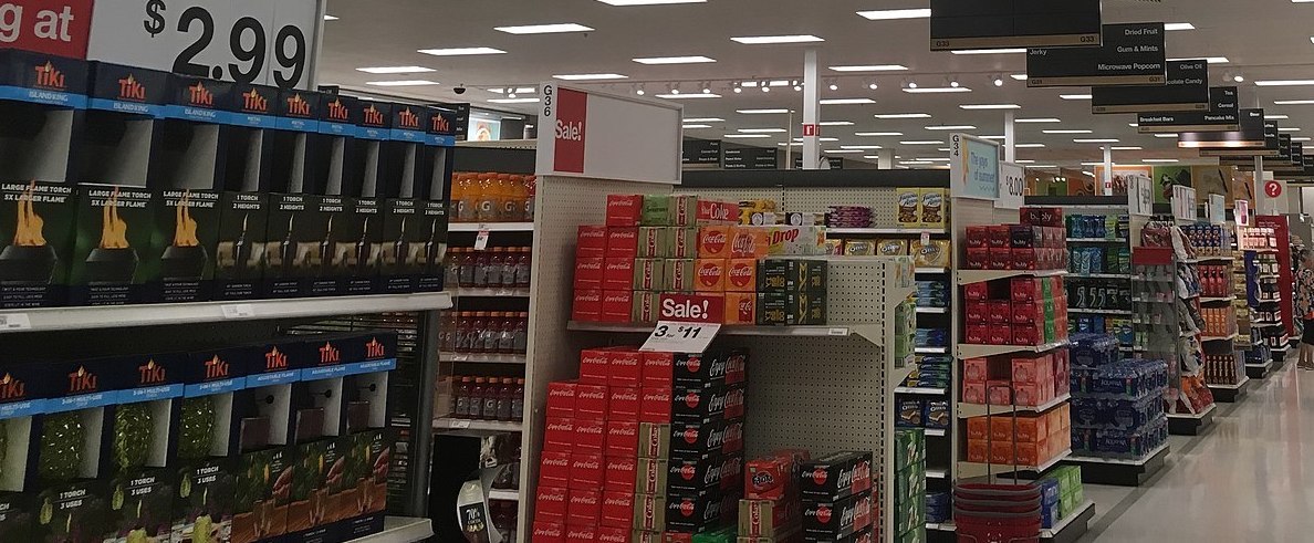 Inside Target view of snack aisles; specifically soda, water, and cookies. A few 'Sale!' posters can be seen throughout the image.
