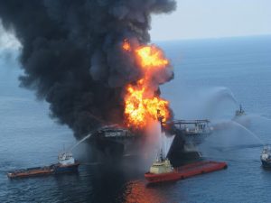 The oil rig Deepwater Horizon on fire in the Gulf of Mexico. Five boats surround it spewing water to put out the fire.
