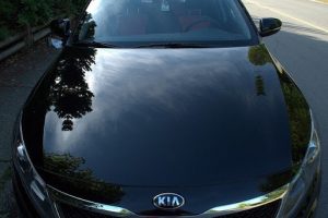 Photo of the hood of a black KIA that reflects the sky.