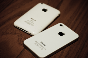 Two white iPhone 4s sitting face down on a wood table.