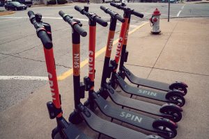 Six electric SPIN scooters sit next to eachother on a sidewalk in Jefferson City.