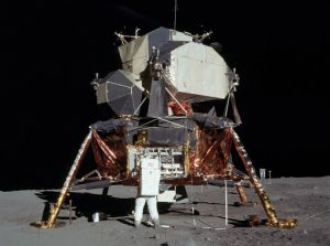 Buzz Aldrin in a spacesuit on the moon removing a piece of equipment from the Lunar Lander.