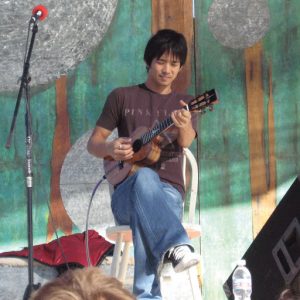 Jake Shimabukuro sitting outside playing a ukulele.