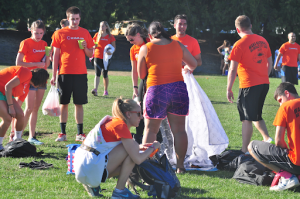 Co-ed adult kickball team wearing matching orange shirts and cleaning up the field. 