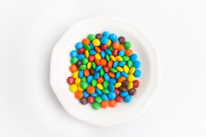 White bowl with lots of M&Ms sits on a white table.