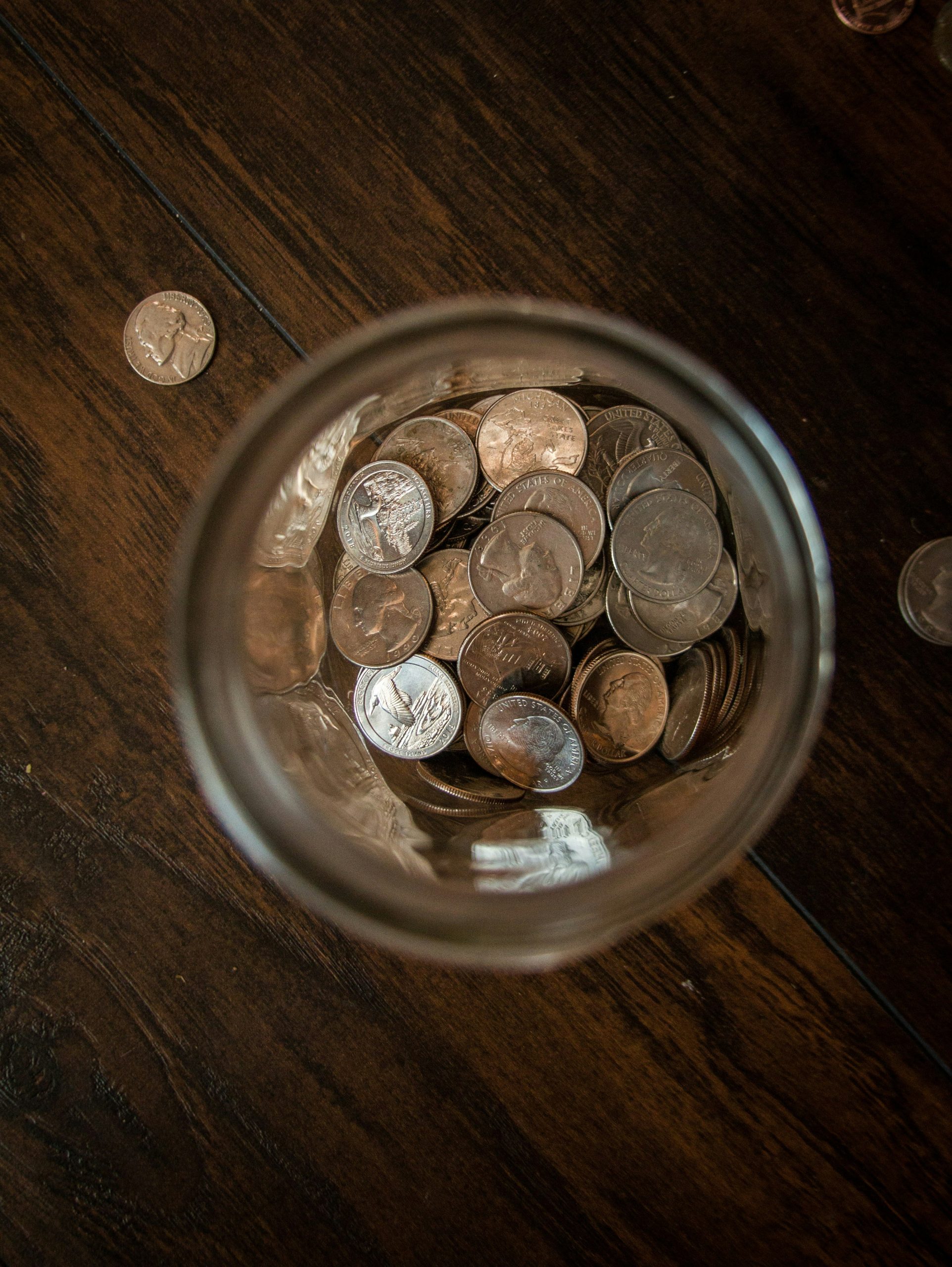 A glass jar of coins sits on a dark wooden table