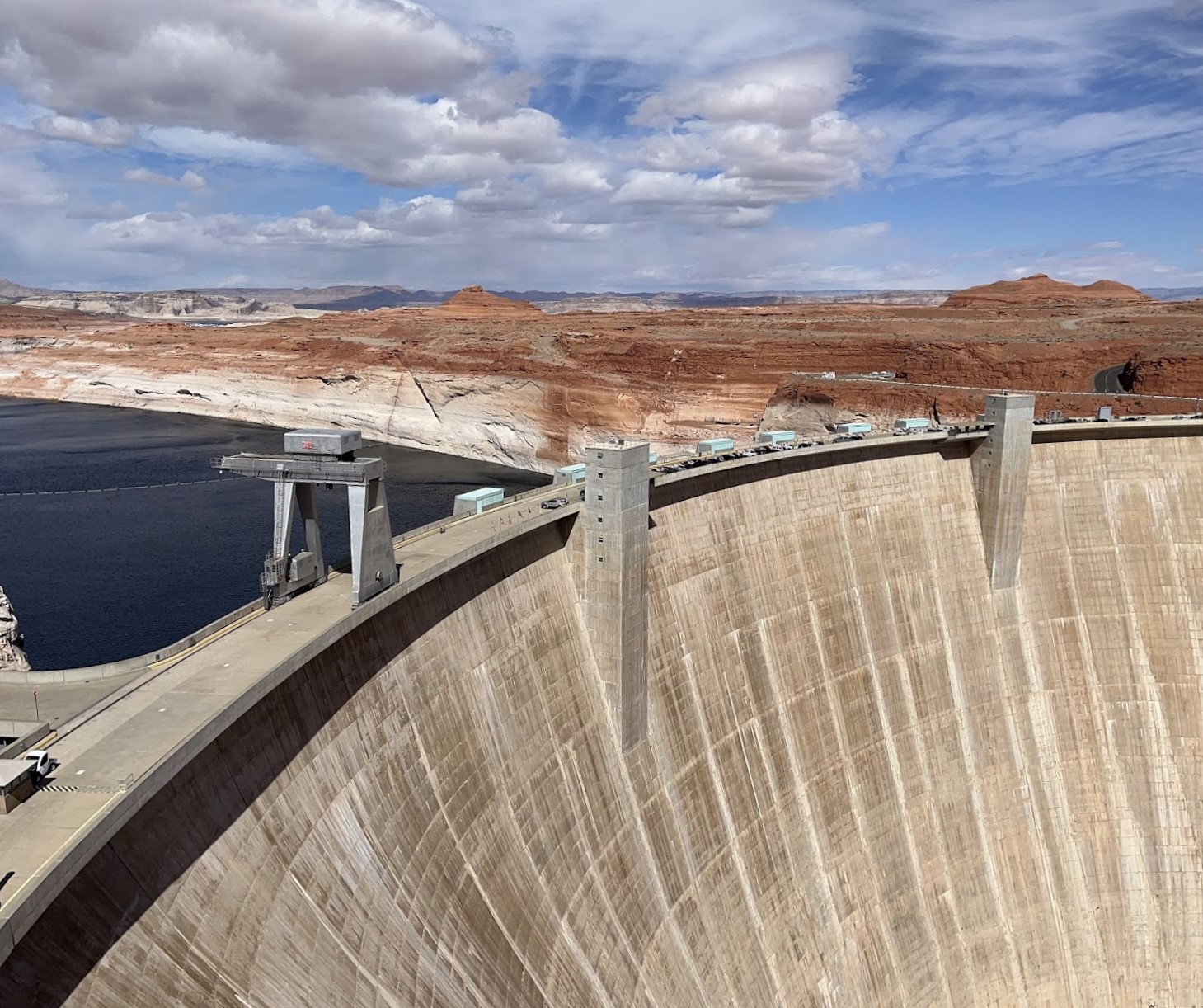 A large tan concrete dam. The water level is much higher behind the dam than in front of it.