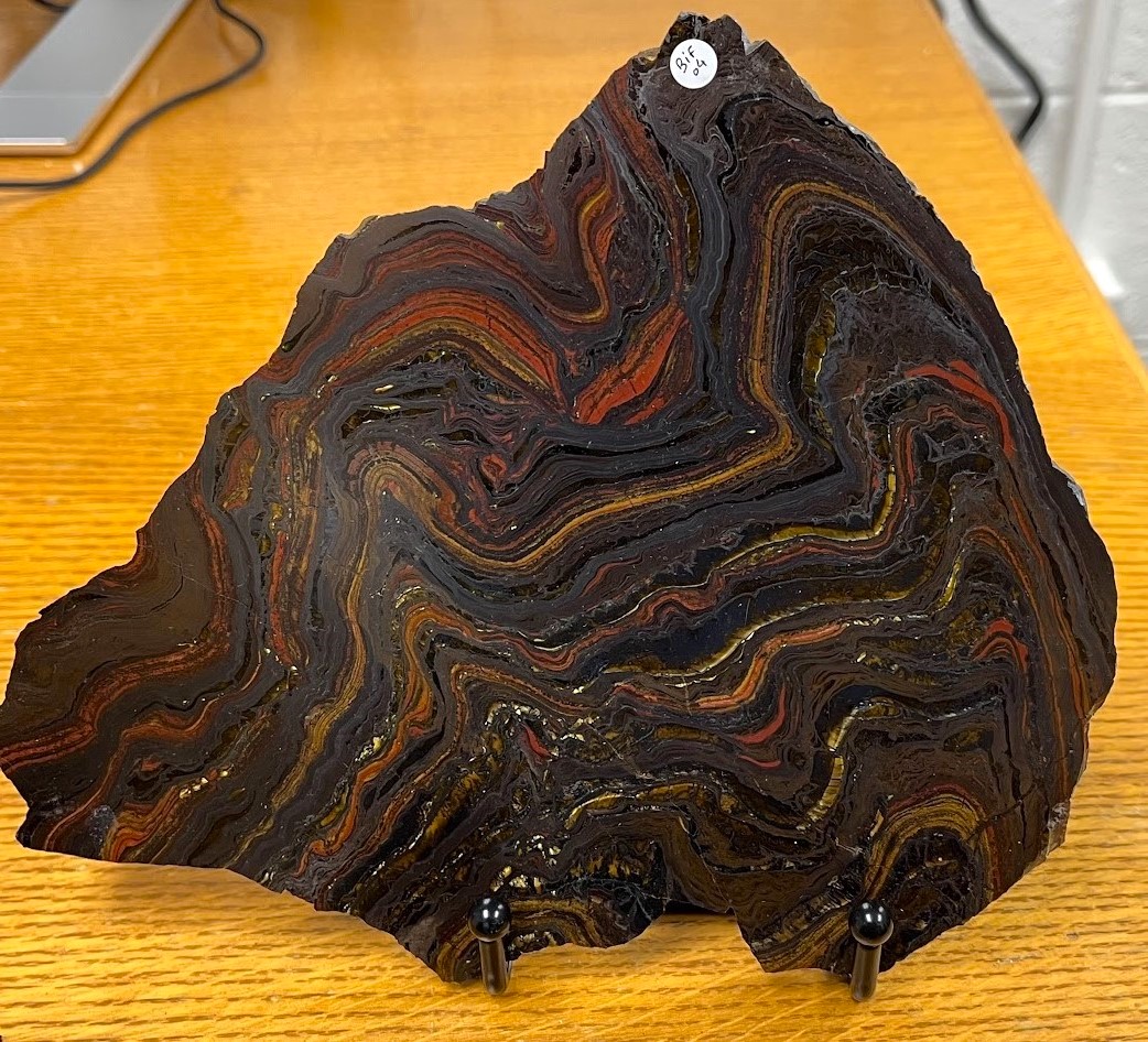 A slice of rock, showing red and brown curvy layers with glittering dots throughout.