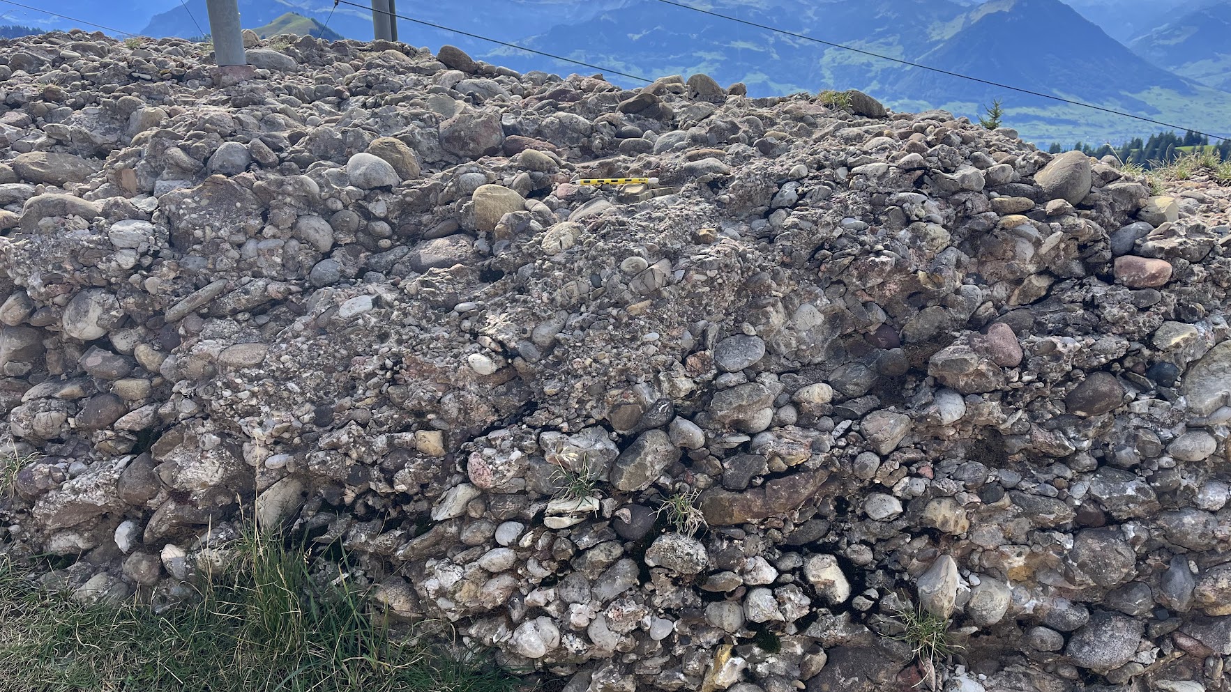 Tan, brown, and white conglomerate with rounded cobbles embedded parallel and stacked on each other in a slanted manner.