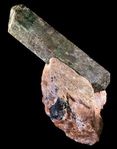 An elongated prismatic crystal of dark green apatite.