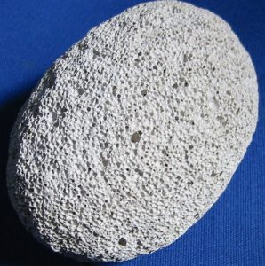 A round-shaped sample of dull white lava rock full of small air holes.