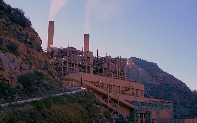 A power plant with steam coming out, surrounded by rocky hills on either side.