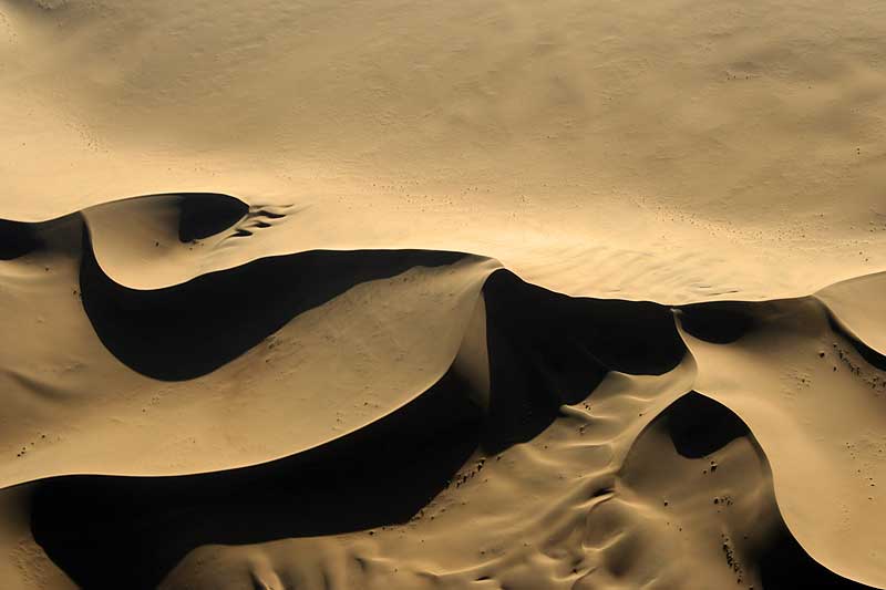 Tan sand dune with a central peak and multiple ridges branching outward in various directions.