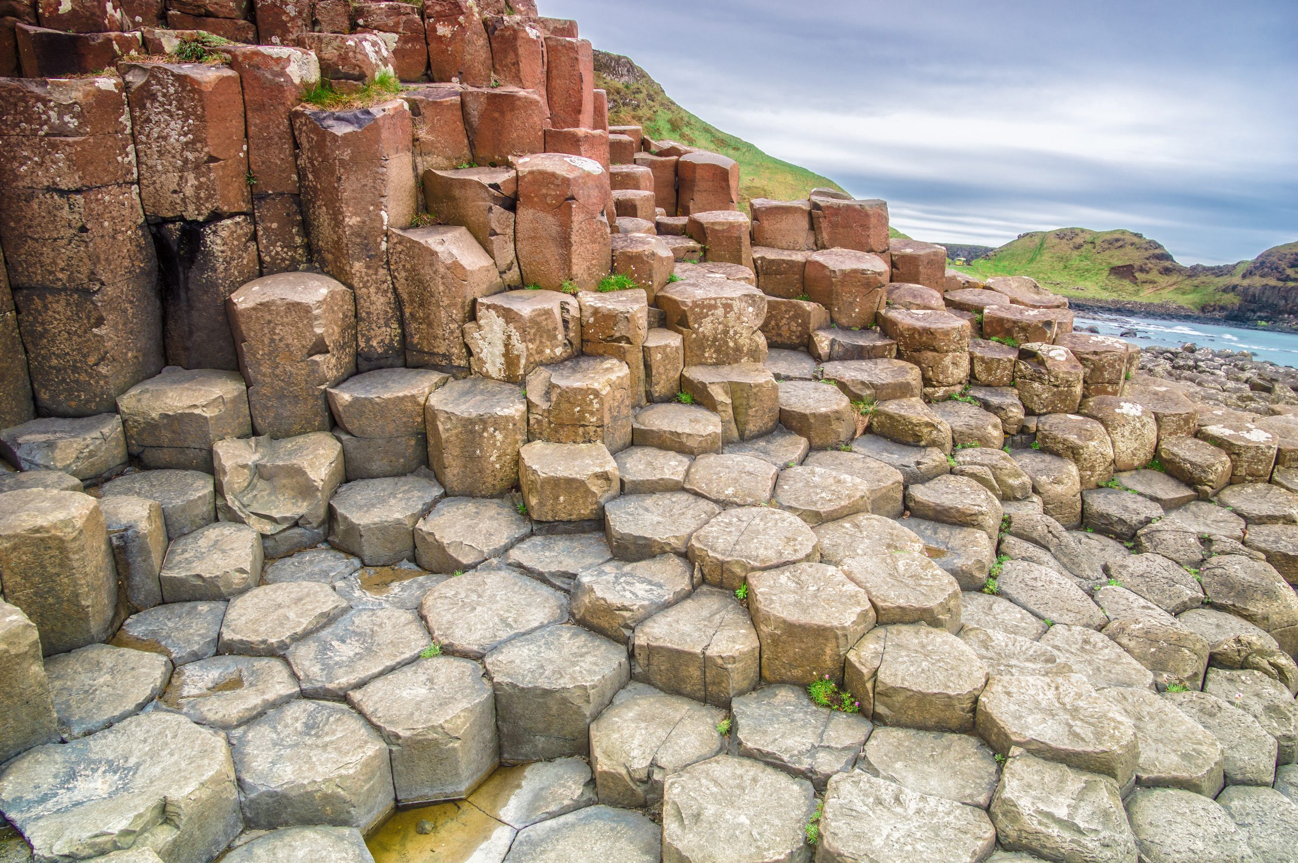 Landscape composed of interlocking hexagonal tan, red, and brown basalt columns that vary in height.