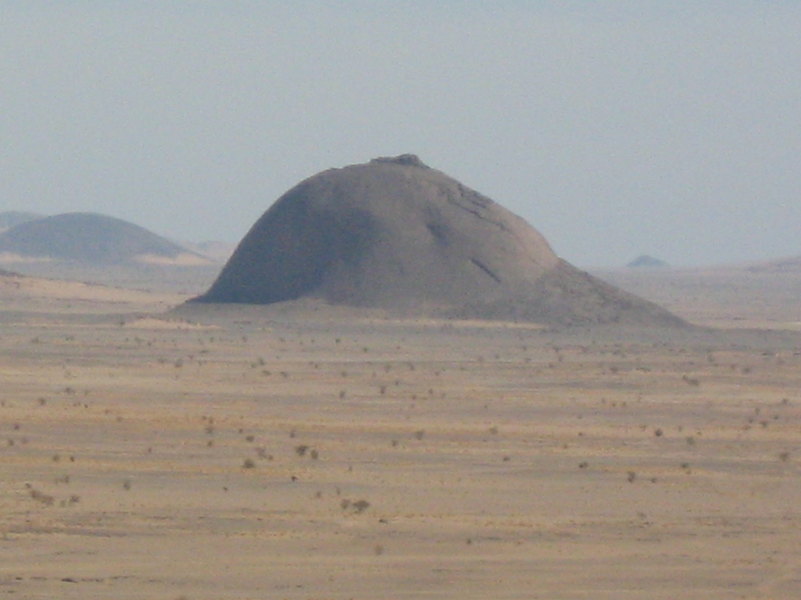 Single dome-shaped mountain rising from a flat desert landscape.