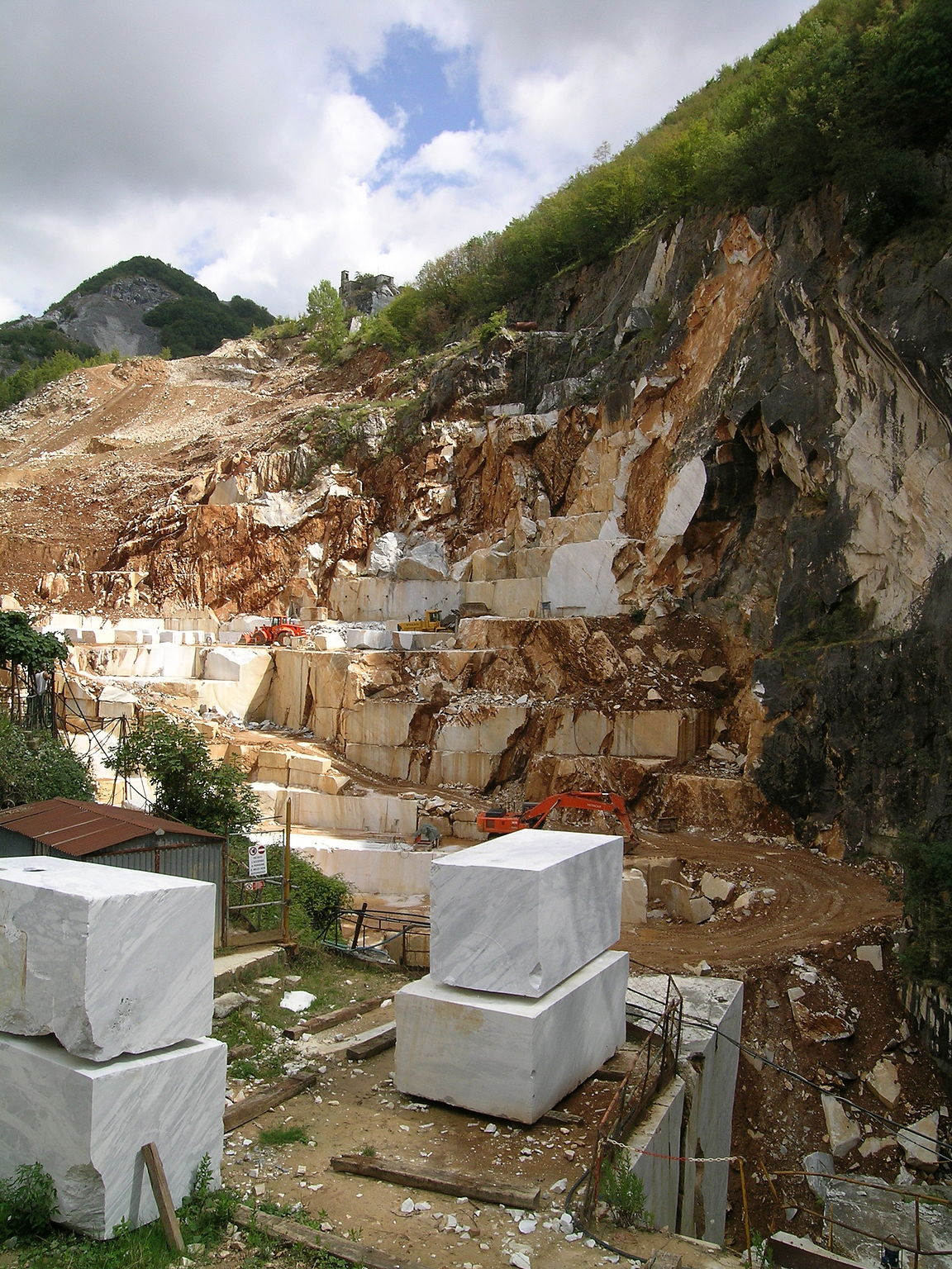 A quarry carved into a hillside with large blocks of gray and white marble removed.