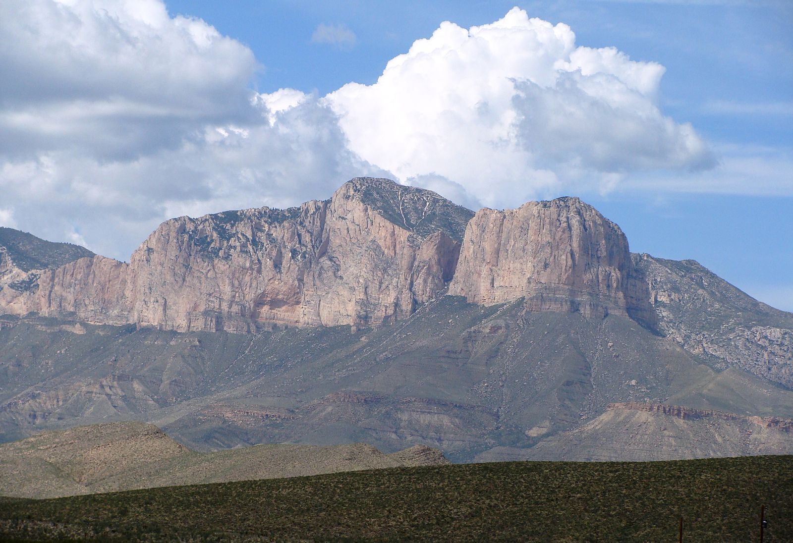 A mountain with steep cliffs rising from vegetation-covered slopes; the mountain has a blunt, nearly flat top.