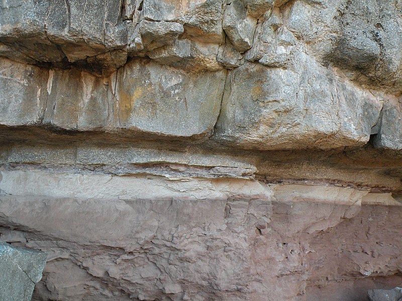 Outcrop of thick beds of flat-lying dull tan rock on top of pink rock with a chalky appearance.