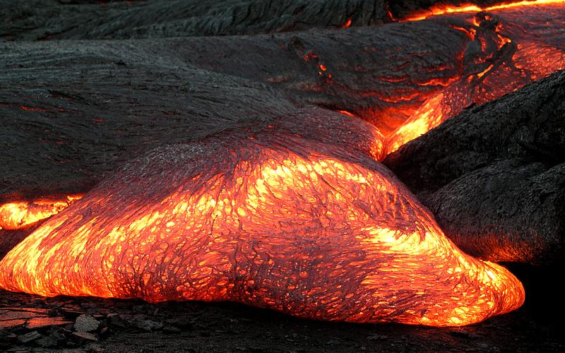 Glowing orange-to-yellow molten lava flowing next to black solid volcanic rock.