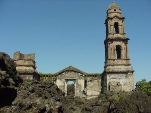 Grayish tan stone church tower and building surrounded by black and brown blocky volcanic rocks.