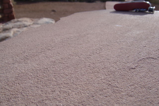 There are slight grooves in a very grainy-looking whitish tan rock; a pocket knife rests on the rock for scale.