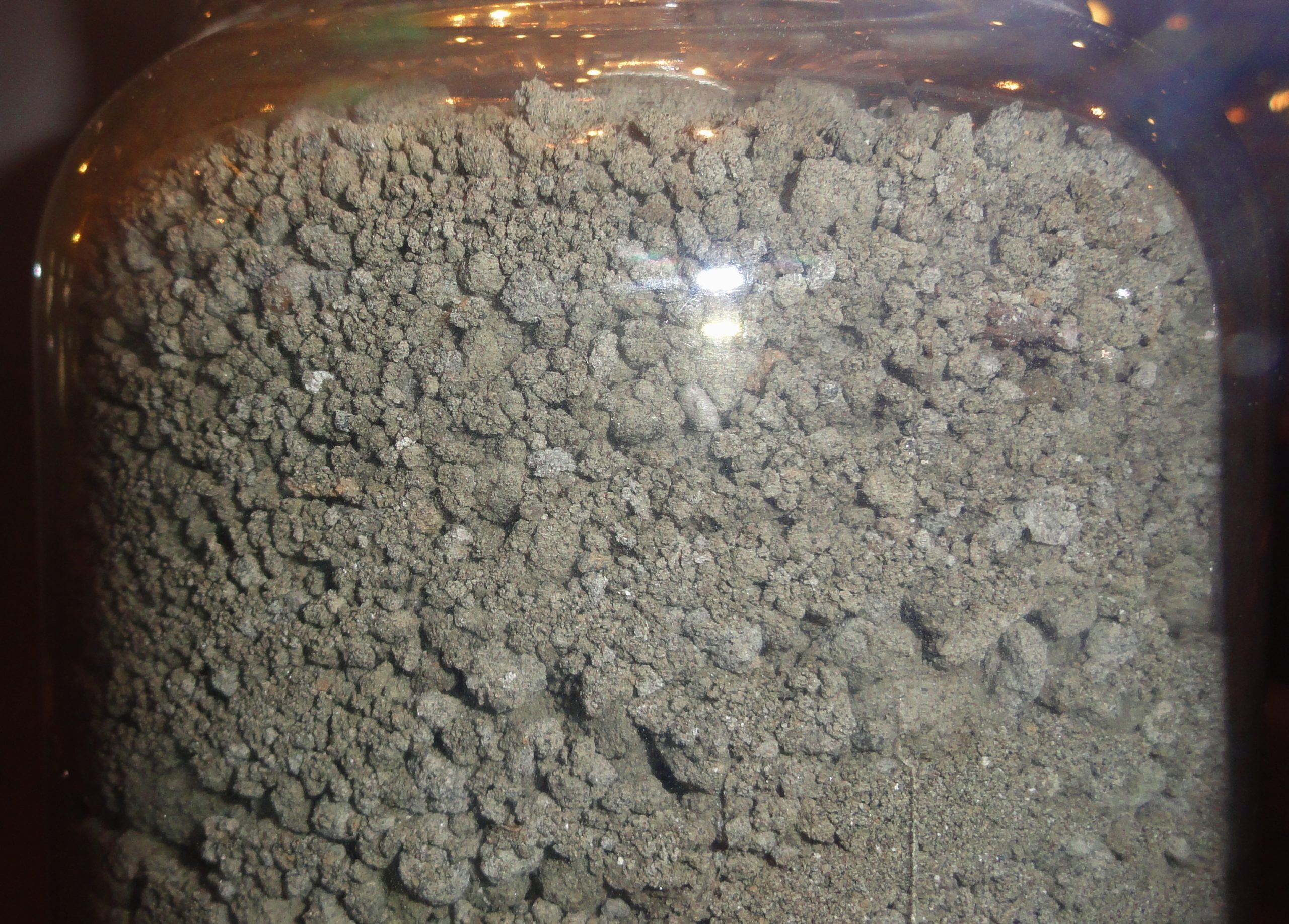 A clear rounded container full of dark gray pebbles and rocks.