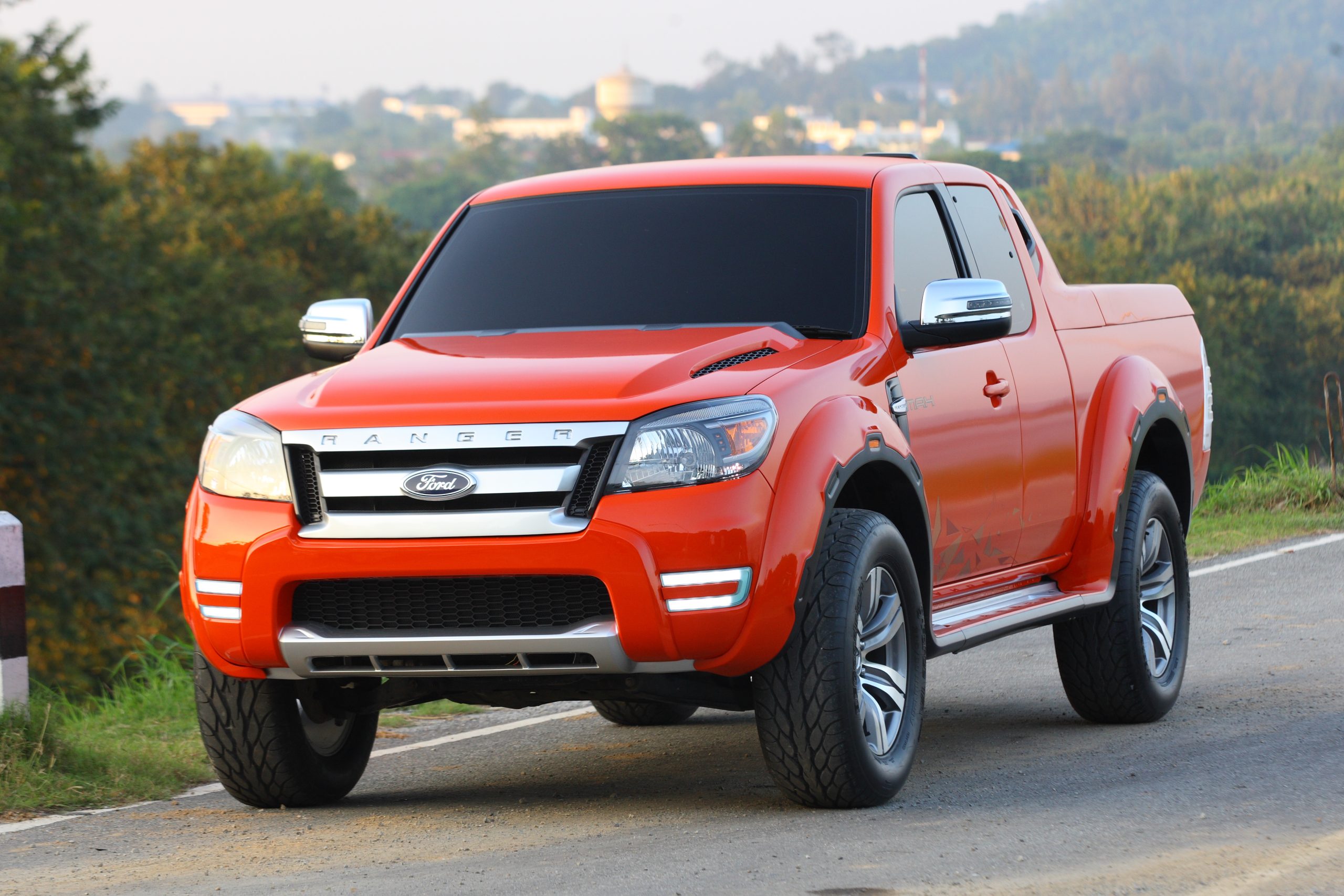 Dark orange pickup truck parked on a rural road with green hills in the background