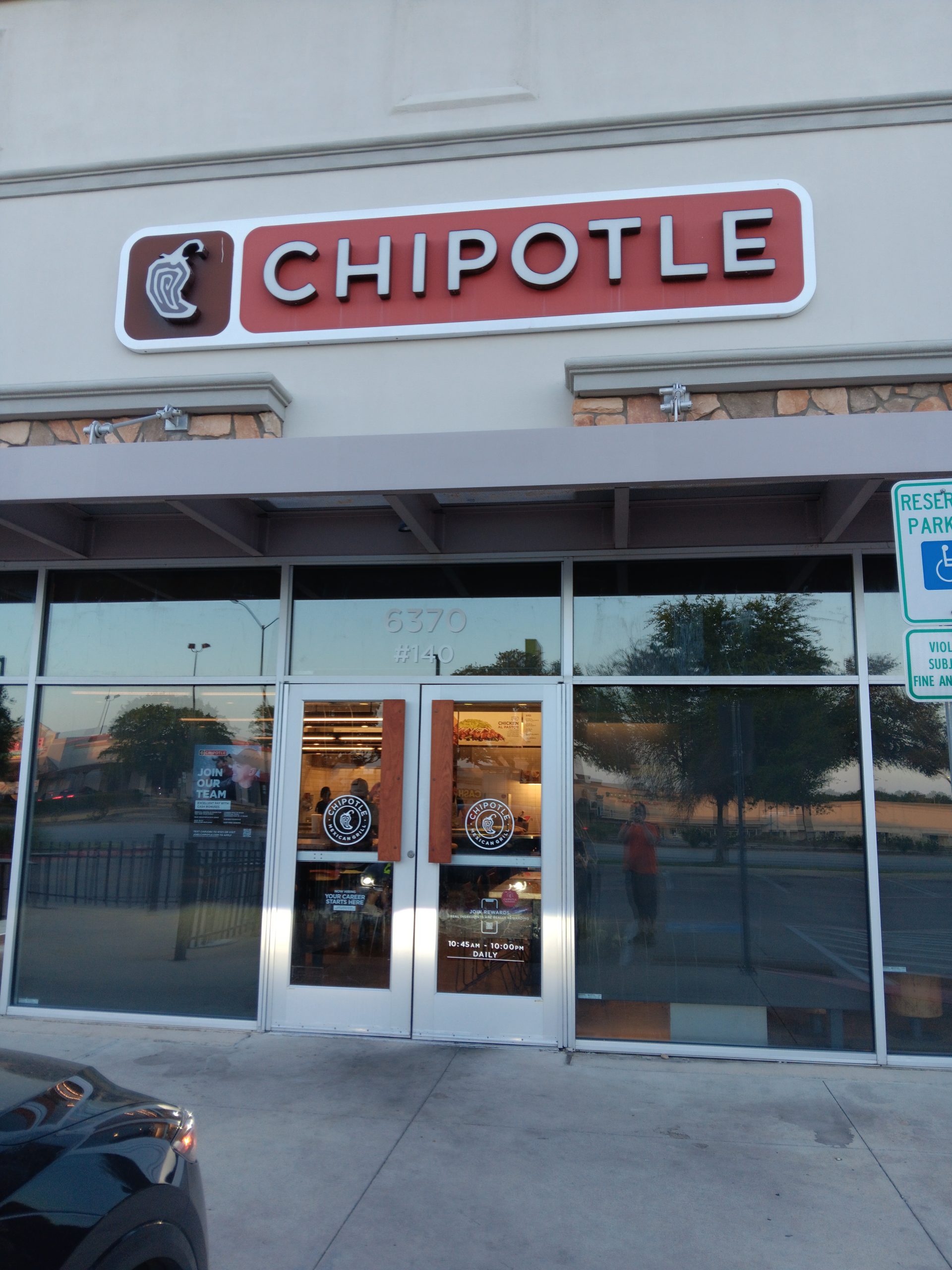 Exterior of a Chipotle restaurant showing a red sign above glass doors and windows