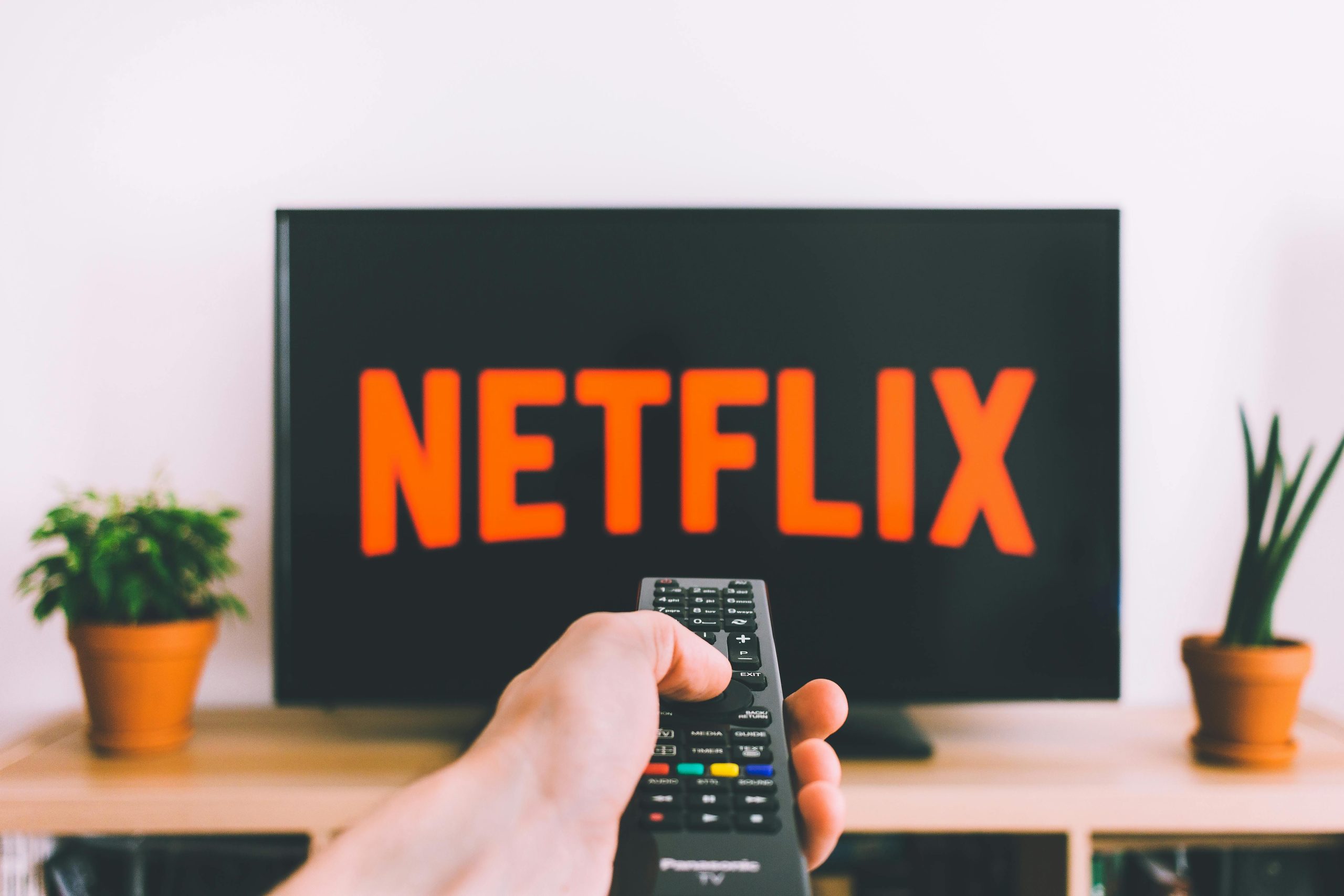 Person's hand holding a remote and pointing it at the screen to watch Netflix