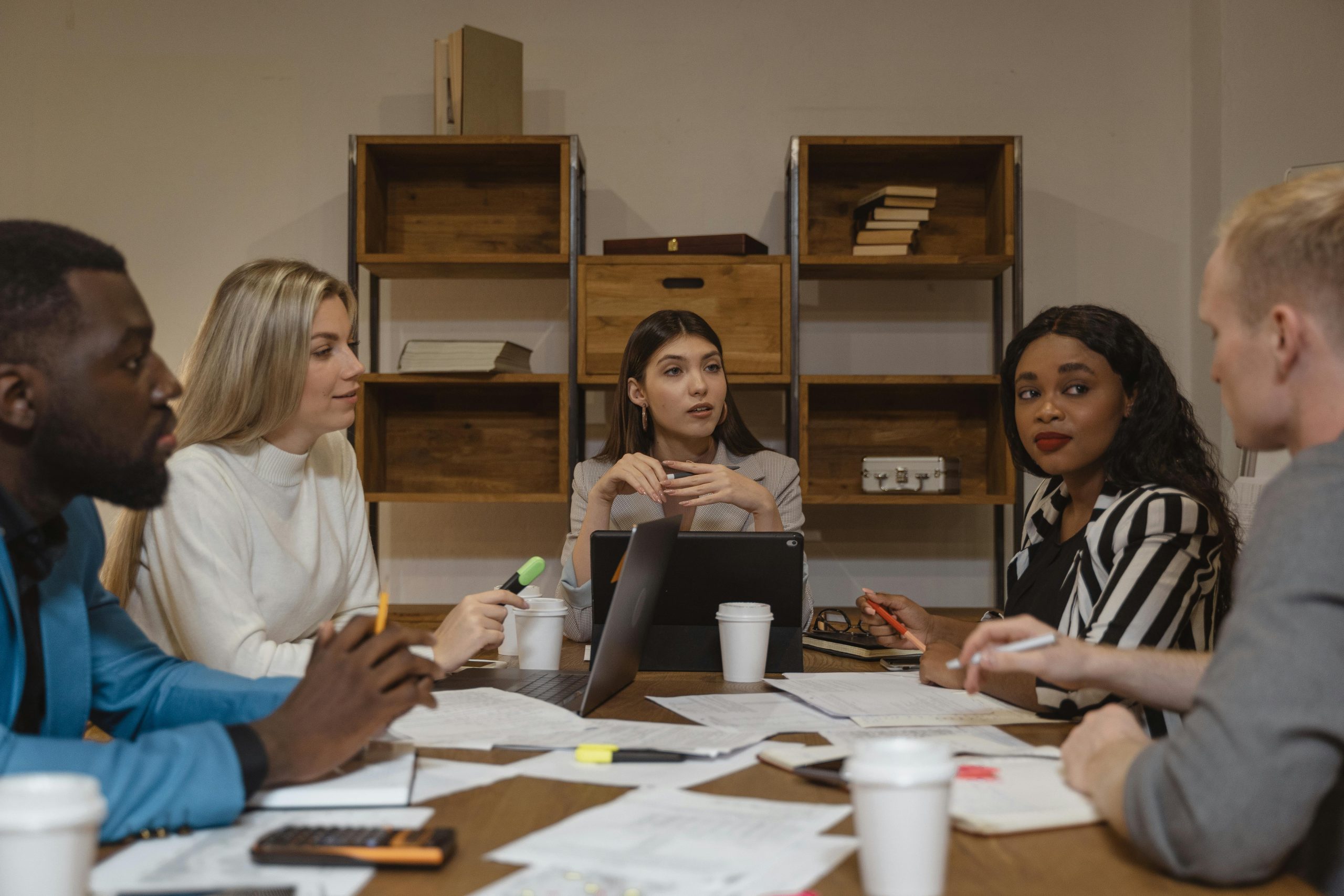 Five young adults sitting around a table with coffee, papers, and calculators