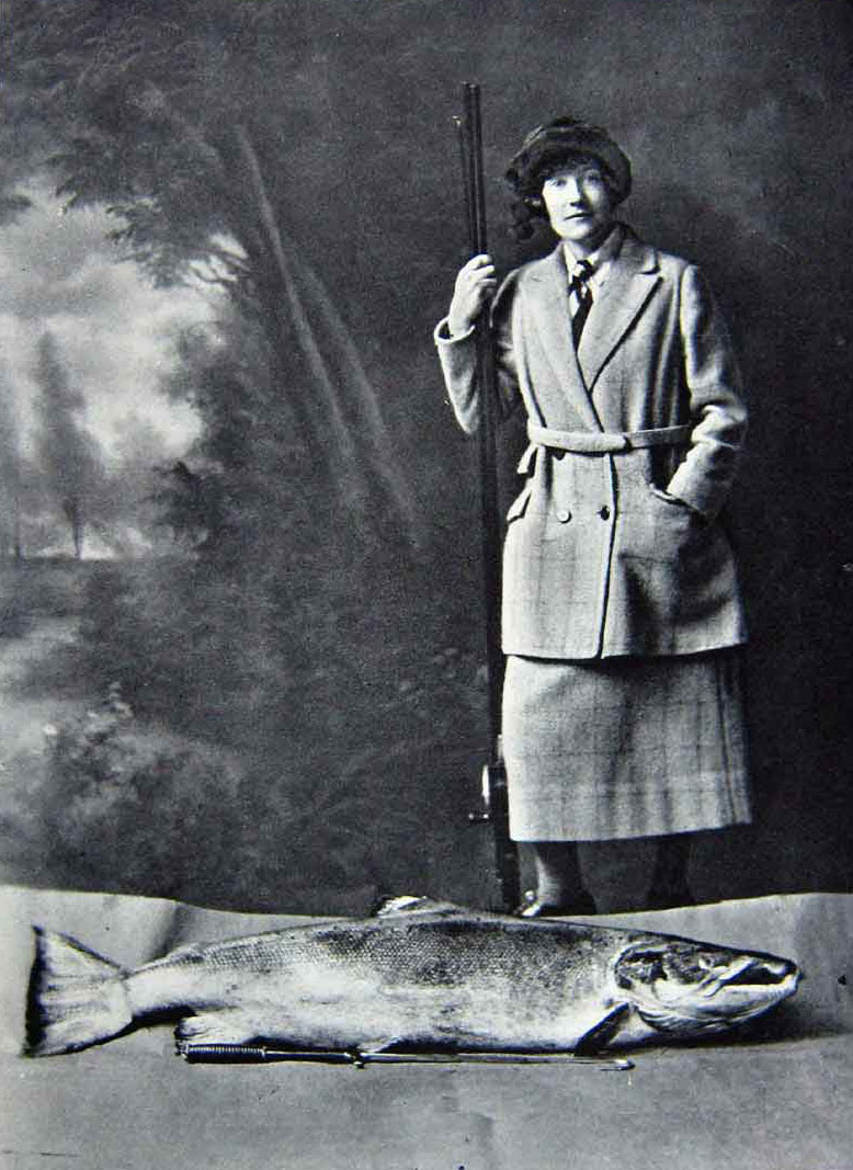 Black and white image of a woman with a fishing rod standing over a large fish