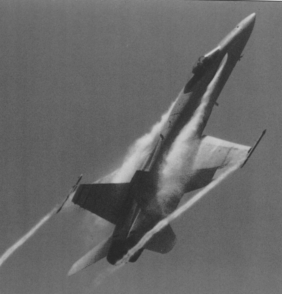 An F-18 in a steep climb is shown with vortices trailing from the wingtips and the fuselage as it climbs.