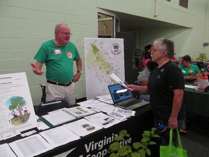 man standing at table with maps and other educational materials speaking to woman holding a green bag