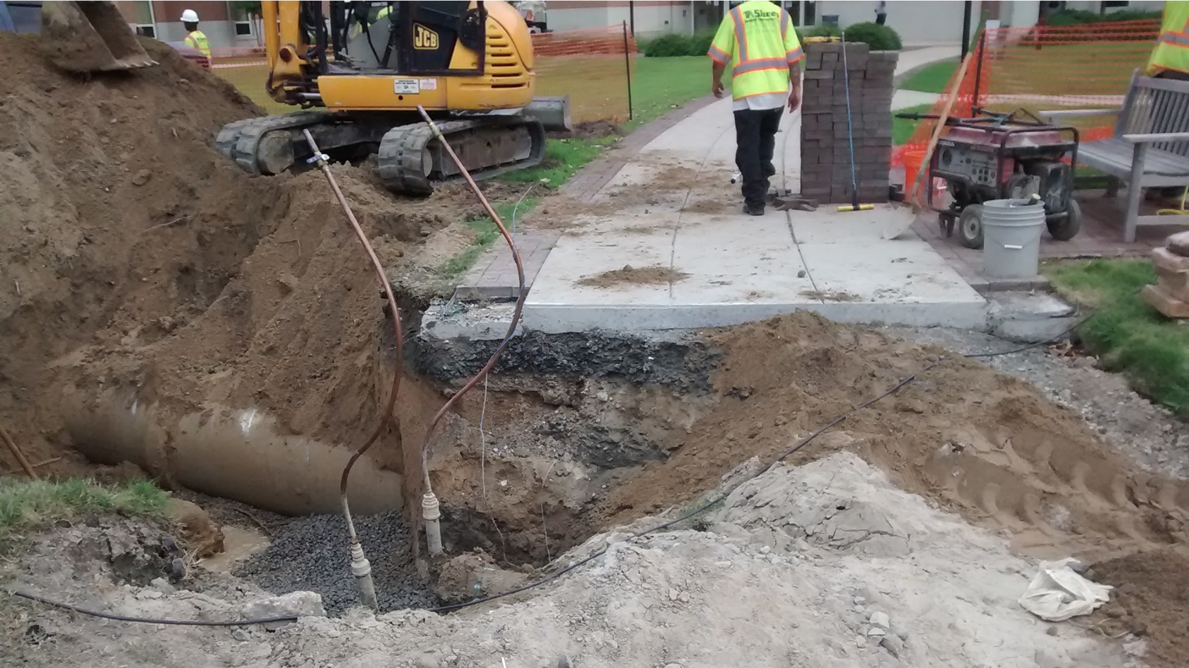 road construction showing different colored dirt. a sidewalk leads away and a worker with a yellow vest walks away