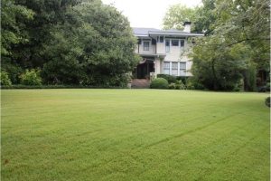 A photograph. A large mowed yard in front of a large two story house, there are many large trees on both sides of the house.