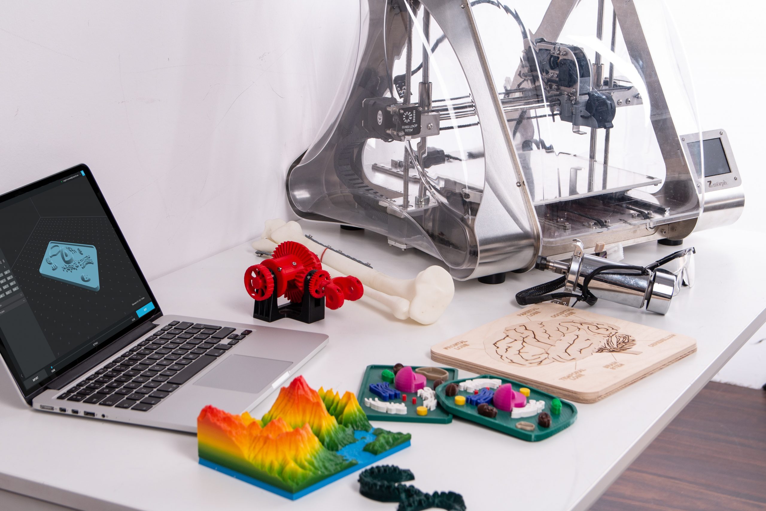 A 3-D printer sits beside a laptop and small colorful plastic pieces.
