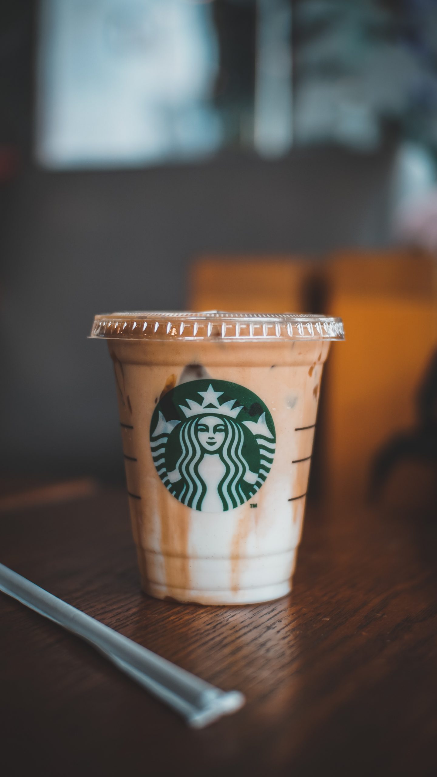 Iced starbucks coffee with cream sits on a wooden table next to a straw.