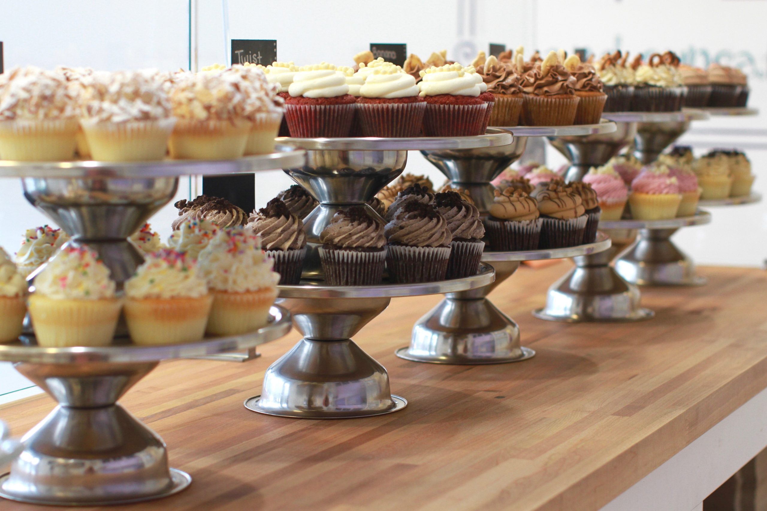 A photograph of a cupcake shop display, showing a variety of small cakes and sweets. Many have intricate toppings and designs.