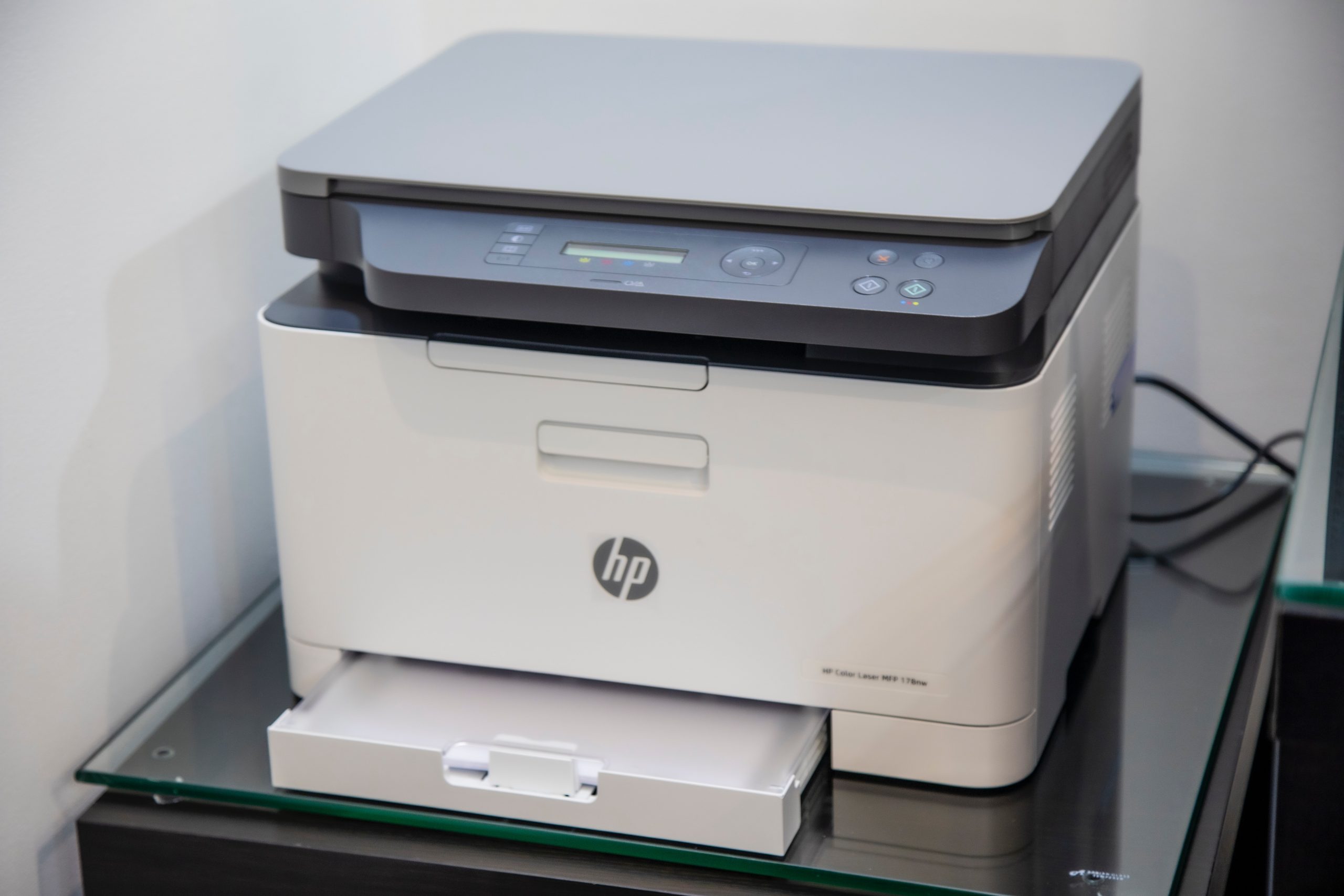 A white HP printer sits on a glasstop table.