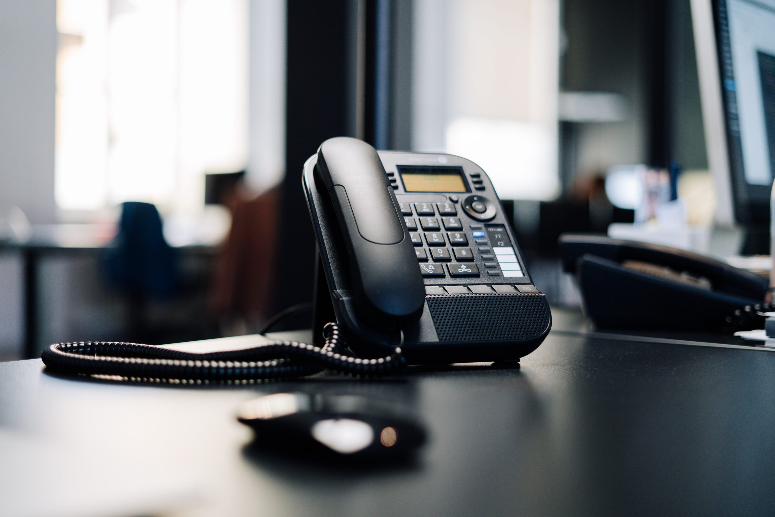 A black landline office phone sits on a black desk.