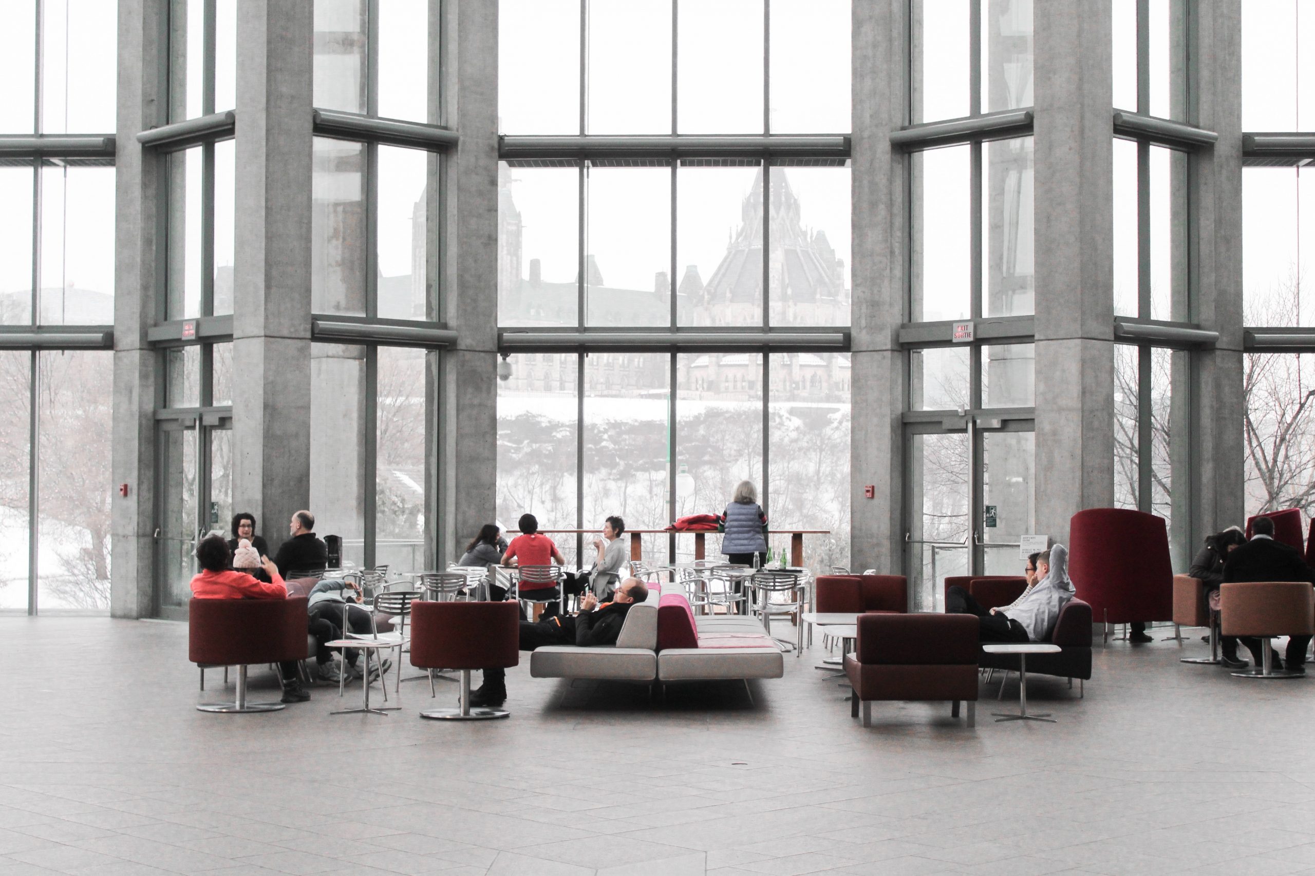 Photo of people sitting on various couches inside of a building with large windows overlooking the snow outside.