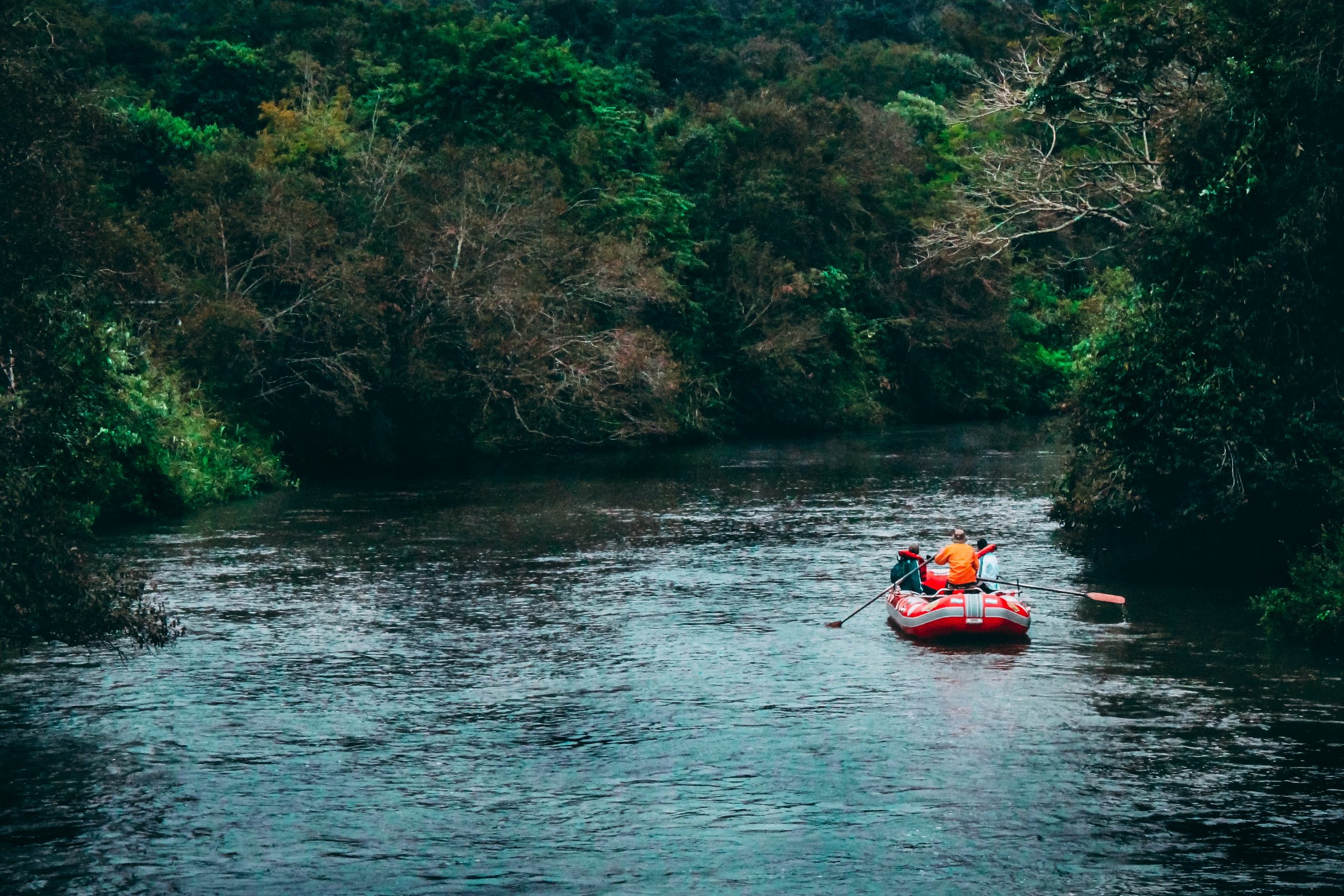 Photo of a few people on a raft on pretty still water. Trees line both sides of the river.