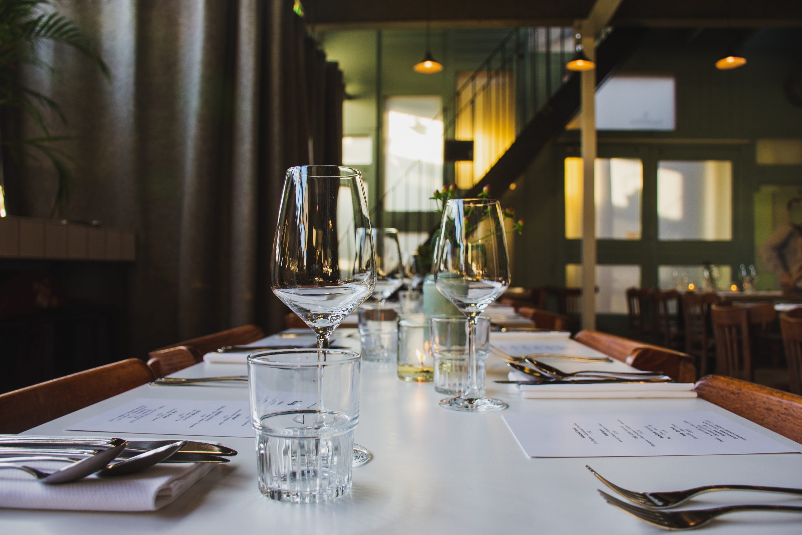 Photo of an indoor restaurant tablescape with clear wine glasses, white linen napkins, and ambient lighting.