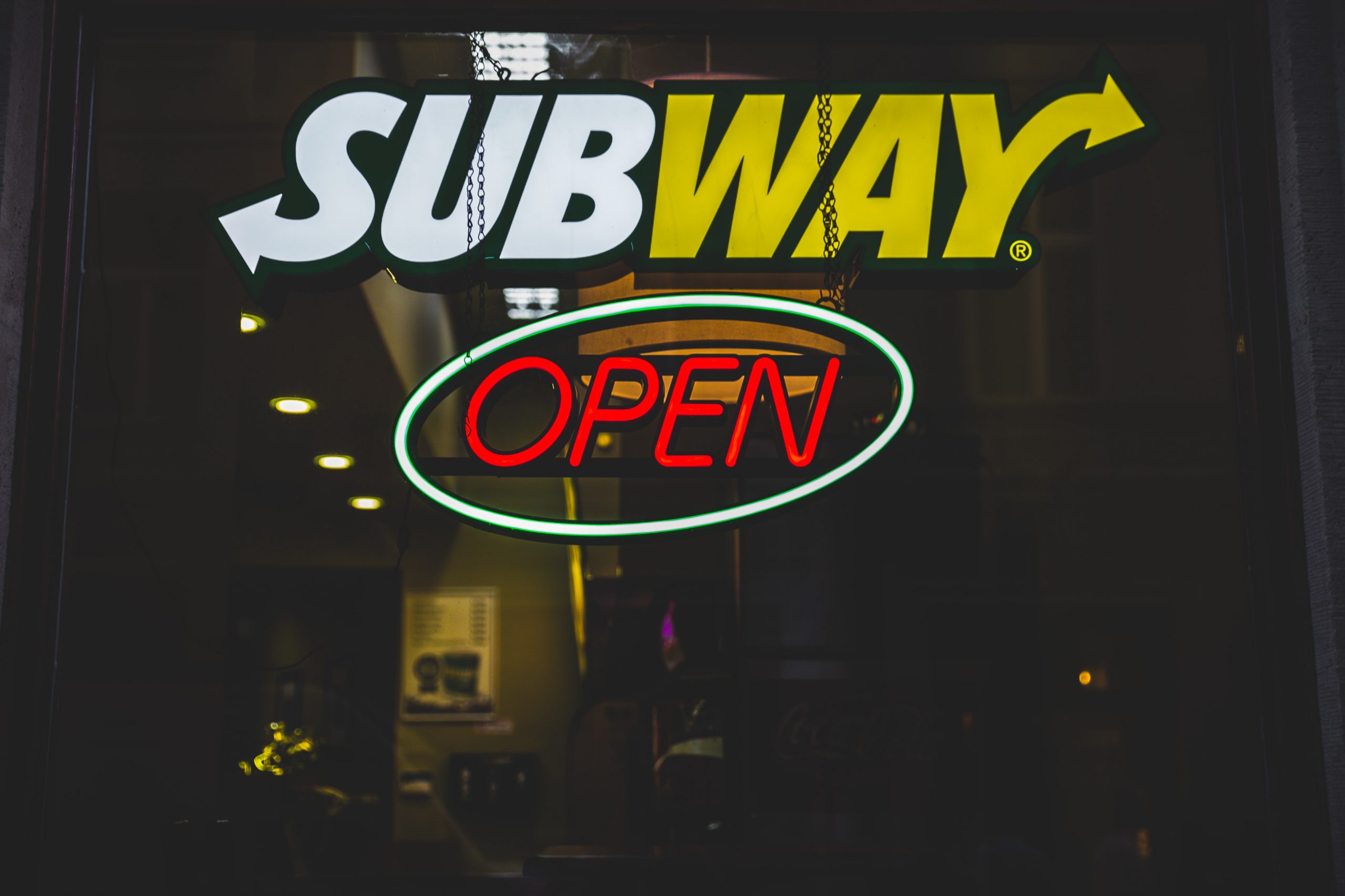 Photograph at night of an illuminated Subway sign above a neon open sign.