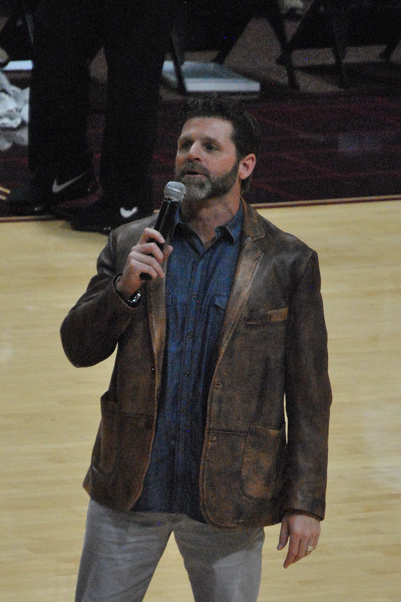 Virginia Tech head football coach Brent Pry holding a microphone standing on the basketball court in Cassell Coliseum.